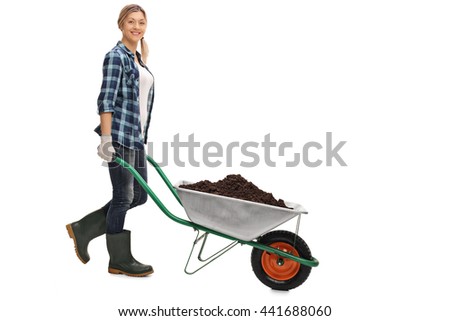 Full length portrait of a young woman pushing a wheelbarrow full of dirt isolated on white background