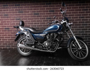 Full Length Profile Of Blue Standard Cruiser Style Motorcycle In Front Of Brick Wall