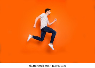 Full length profile photo of attractive crazy youngster jump high rush sale shopping center addicted shopper wear striped t-shirt jeans shoes isolated bright orange color background - Shutterstock ID 1689831121