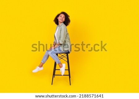 Full length profile photo of brunette lady sit on chair look up wear shirt jeans boots isolated on yellow background