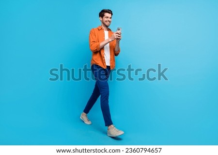 Full length profile photo of cheerful nice man hold use smart phone texting typing post isolated on blue color background