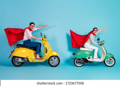 Full length profile photo of crazy lady guy drive two retro moped raise fists wear red cape cloak mask rushing road party super heroes role coat fly air isolated blue color background
