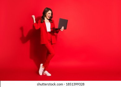 Full Length Profile Photo Of Cute Young Girl Hold Laptop Raise Fist Up Wear Blazer Trousers Sneakers Isolated Red Color Background