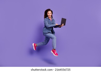 Full length profile photo of energetic sporty person hold use wireless netbook jump running isolated on violet color background