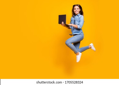 Full length profile photo of funny business lady jump high up hold notebook hands addicted worker always online wear casual denim outfit white sneakers isolated yellow color background