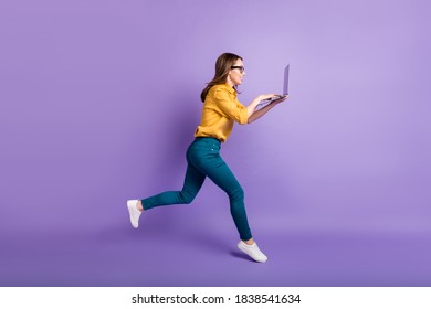 Full length profile photo of girl run hold pc typing touchpad wear yellow shirt blue pants sneakers isolated violet color background - Powered by Shutterstock