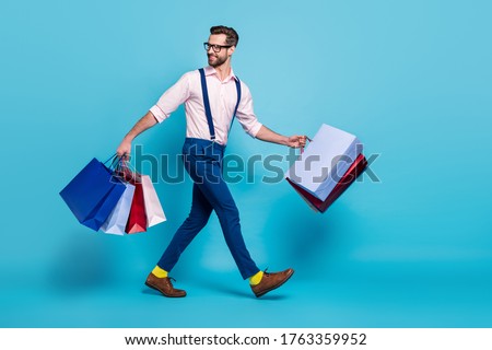 Full length profile photo of handsome business man carry many bags buy vacation stuff shopping center good mood wear specs shirt suspenders pants boots isolated blue color background