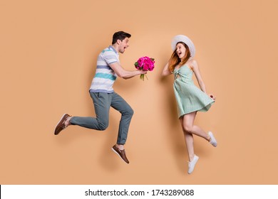 Full length profile photo of pretty lady handsome guy excited married couple traveling jump high taking fresh bunch flowers wear summer clothes sun hat isolated beige color background
