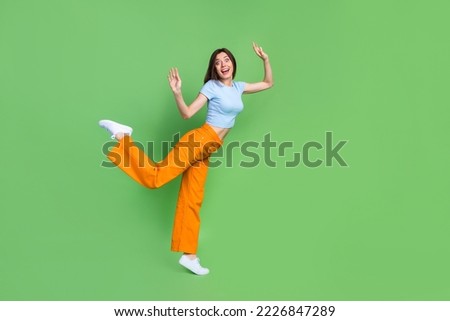 Full length profile photo of satisfied overjoyed person standing one leg raise hands isolated on green color background