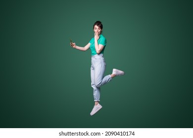 Full Length Profile Photo Of Shocked Woman Jumping High Up Hold Telephone While Looking At Camera Isolated Over Green Color Background