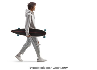 Full length profile shot of an african american guy carrying a longboard and walking isolated on white background    