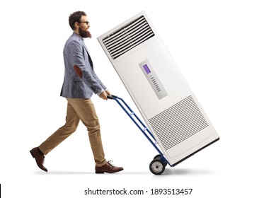 Full Length Profile Shot Of A Bearded Man Pushing A Hand-truck With A Portable Self Standing Ac Unit Isolated On White Background