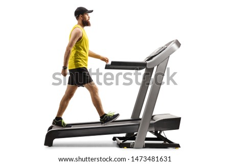 Full length profile shot of a bearded guy in sportswear walking on a treadmill with an incline isolated on white background