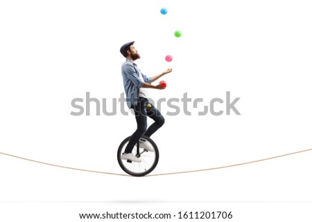 Full length profile shot of a bearded male hipster juggler with balls riding a unicycle on a rope isolated on white background