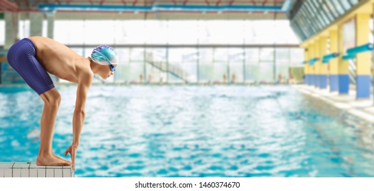 Full length profile shot of a boy swimmer on the start position at a swimming pool