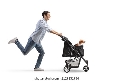 Full Length Profile Shot Of A Casual Young Man Pushing A Dog Stroller And Running Isolated On White Background