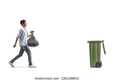 Full Length Profile Shot Of A Casual Young Man Walking Towards A Bin And Carrying A Plastic Garbage Bag Isolated On White Background