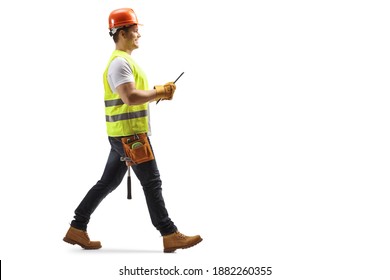 Full length profile shot of a construction worker with a helmet and tool belt holding a document and walking isolated on white background - Powered by Shutterstock