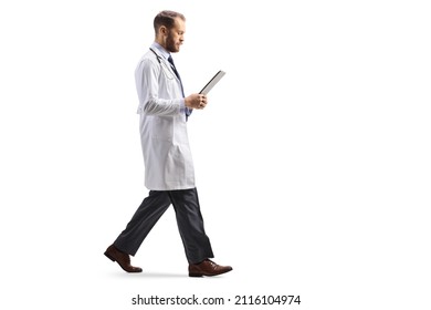 Full Length Profile Shot Of A Doctor Walking And Looking At A Document Isolated On White Background