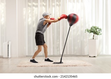 Full Length Profile Shot Of An Elderly Man With Punching A Free Stnading Boxing Bag At Home