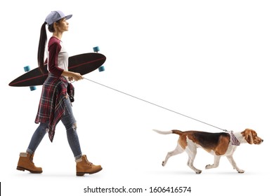 Full length profile shot of a female teenager with a skateboard walking a dog isolated on white background