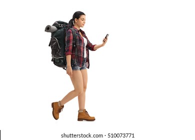 Full Length Profile Shot Of A Female Hiker Walking And Looking At A Cell Phone Isolated On White Background