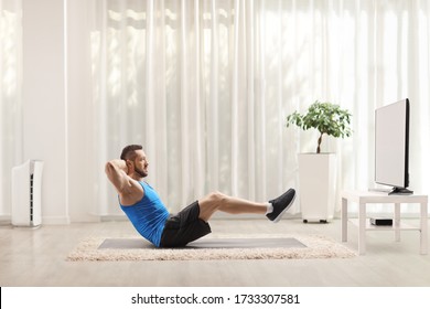 Full Length Profile Shot Of A Fit Young Man Doing Abs Workout On Floor In Front Of A Tv At Home