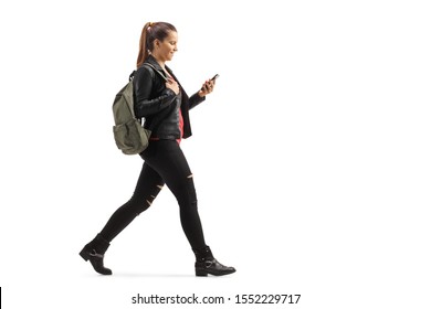 Full Length Profile Shot Of A Girl With A Backpack Walking And Looking At Her Mobile Phone Isolated On White Background