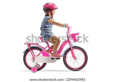 Full length profile shot of a girl with a helmet riding a pink bicycle with training wheels isolated on white background