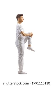 Full Length Profile Shot Of A Guy In White Clothes Streching Leg Isolated On White Background