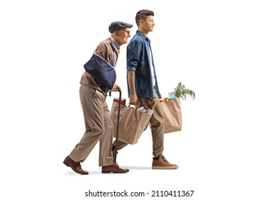 Full length profile shot of a guy carrying grocery shopping bags for an elderly man with a broken arm isolated on white background - Powered by Shutterstock