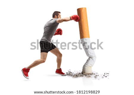 Full length profile shot of a guy punching a cigarette with boxing gloves isolated on white background