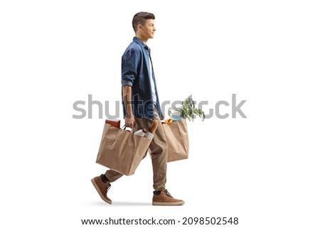 Full length profile shot of a guy carrying grocery bags and walking isolated on white background