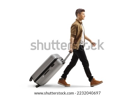 Full length profile shot of a guy walking and pulling a suitcase isolated on white background