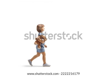 Full length profile shot of a little girl walking and holding a teddy bear isolated on white background