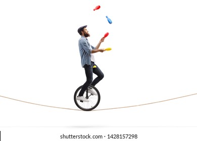 Full length profile shot of a male juggler with clubs riding a unicycle on a rope isolated on white background