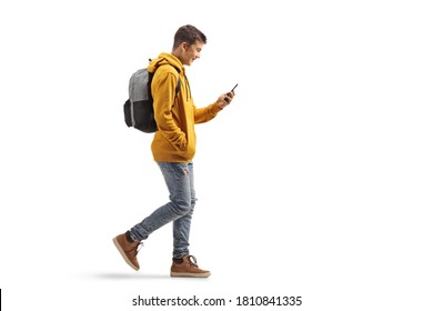 Full Length Profile Shot Of A Male Teenage Student Walking And Looking At A Mobile Phone Isolated On White Background