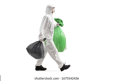 Full length profile shot of a man wearing a protective suit and walking with waste bags isolated on white background
