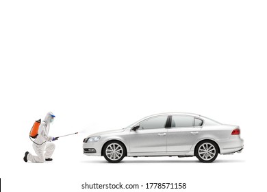 Full length profile shot of a man in a hazmat suit kneeling and disinfecting a car isolated on white background