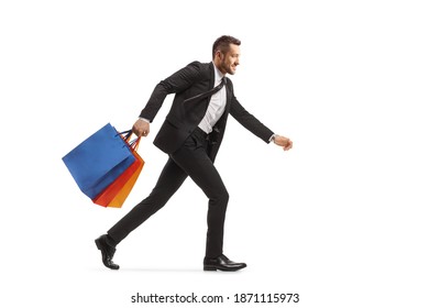 Full Length Profile Shot Of A Man In A Black Suit Running And Carrying Shopping Bags Isolated On White Background