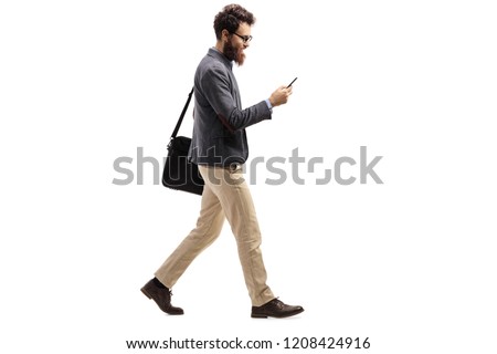 Full length profile shot of a man walking and looking into a mobile phone isolated on white background