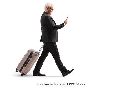 Full length profile shot of a mature businessman walking and pulling a suitcase while using a smartphone isolated on white background - Powered by Shutterstock