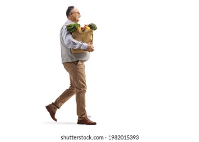 Full Length Profile Shot Of A Mature Man Walking With A Grocery Bag Isolated On White Background