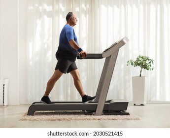 Full Length Profile Shot Of A Mature Man Walking On A Treadmill Inside A Room