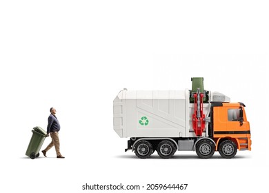 Full Length Profile Shot Of A Mature Man Pulling A Plastic Waste Bin Towards A Garbage Truck Isolated On White Background