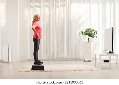 Full Length Profile Shot Of A Mature Woman Standing On An Aerobic Stepper In Front Of Tv At Home