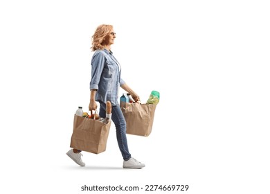 Full length profile shot of a mature woman carrying grocery bags and walking isolated on white background