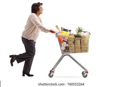 Full Length Profile Shot Of A Mature Woman Running And Pushing A Shopping Cart Filled With Groceries Isolated On White Background