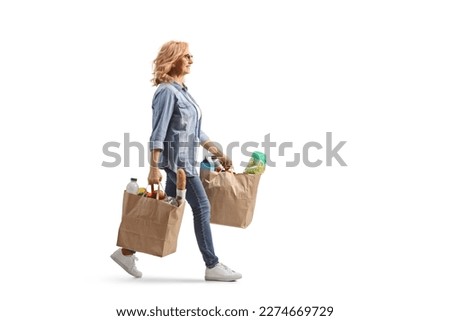 Full length profile shot of a mature woman carrying grocery bags and walking isolated on white background