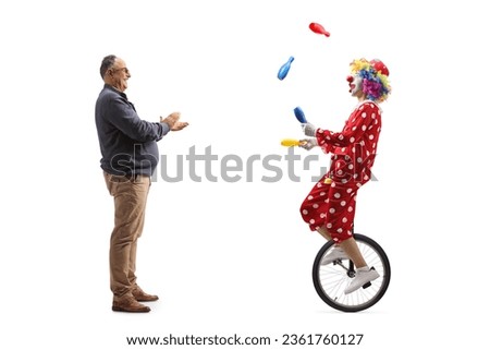 Full length profile shot of a mature man giving an applause to a clown riding a unicycle and juggling isolated on white background